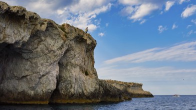 Person fishing from a rocky cliff under a cloudy sky, boat trip around the island of Ortigia, Isola