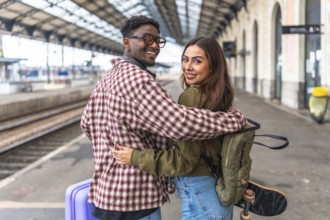 Young multi ethnic couple of tourists hugging at the train station, ready to start their vacation