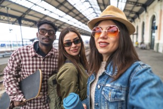 Three happy multi ethnic friends taking selfie at train station before starting their travel