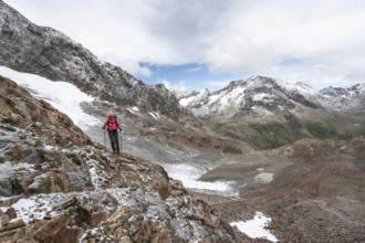 Mountaineer on a rocky hiking trail in a steep rocky mountain landscape with fresh snow in summer,