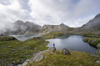 Mountaineer on a rock in front of mountain lakes Wangenitzsee and Kreuzsee, cloudy mountain peaks