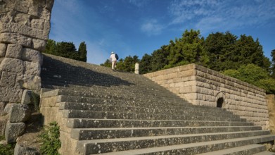 Stone staircase leads to a ruin surrounded by trees, a person climbs the steps, open staircase to