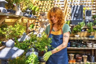 Female gardener wearing gloves, carefully holding a small bonsai tree while tending to plants in a