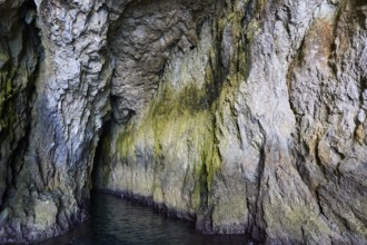 Entrance to a dark cave with irregular rock structures, boat trip around the island of Ortigia,