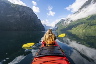 Kayak trip on the Geirangerfjord, young woman paddling in a red kayak, atmospheric fjord landscape,