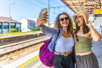 Two happy female tourists are taking a selfie with smartphone at a train station, ready for their