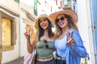 Two happy female tourists wearing summer hats are gesturing the peace sign while enjoying their