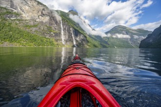 Kayak trip on the Geirangerfjord with waterfall The Seven Sisters, tip of a red kayak in the fjord,