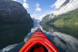 Kayak trip on the Geirangerfjord, tip of a red kayak in the fjord with reflection, atmospheric