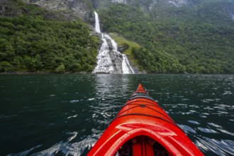 Kayak trip on the Geirangerfjord at the Freier waterfall, tip of a red kayak in the fjord,