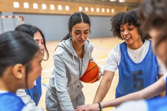 Female basketball coach motivating and inspiring her team during a time out, holding the ball and