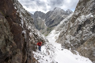 Mountaineer on a rope-secured path in a steep rocky mountain landscape with fresh snow in summer,