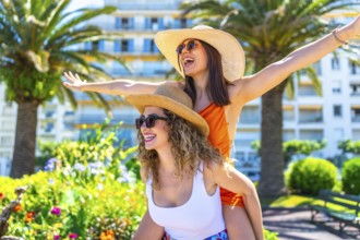 Two cheerful female friends are having fun on vacation in cannes, with one giving the other a