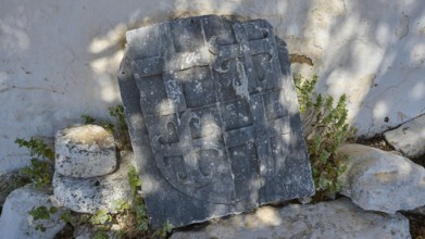 Ancient tombstone with inscriptions, surrounded by vegetation and shade, Church of Agia Paraskevi,