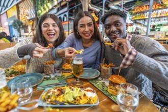 Cheerful multi ethnic friends enjoying a meal together, sharing nachos, burgers, fries, and beer in