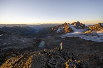 Mountaineer in front of picturesque high mountain landscape at sunrise with alpenglow, blue glacial
