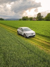 A car drives next to vast fields along a rural road under a cloudy sky, Deer E- CarSharing, Renault