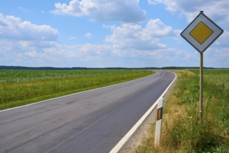 Empty, winding road with traffic sign and wide sky with clouds, Hausen, Würzburg district,