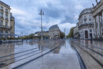 Comedie square in bordeaux city center with wet tram tracks reflecting surrounding buildings on a