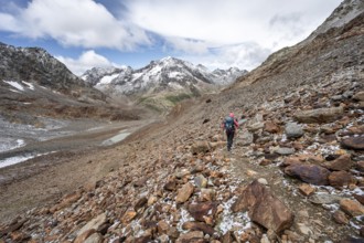 Mountaineer on hiking trail in steep rocky mountain landscape with fresh snow in summer, mountain