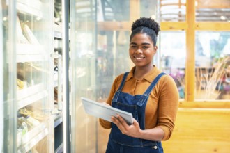 Young supermarket employee using a digital tablet while checking stock in a refrigerated section