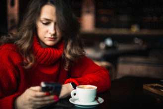 Woman in red sweater focused on her smartphone at a cafe with coffee