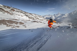 An athlete male skier jumps from a snow-covered slope against the backdrop of a mountain landscape