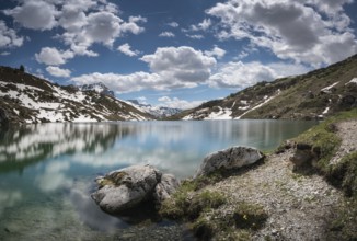 gorgeous mountain lake in the Alps with reflections and snow remnants under a blue sky with white