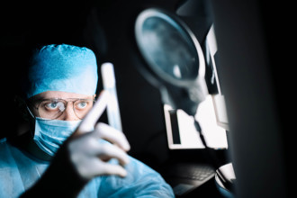 A surgeon in an operating room intently examining a test tube under a magnifying glass
