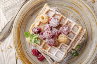 Flat lay view at Belgian waffles served with raspberries and mint leaf dusted with powdered sugar