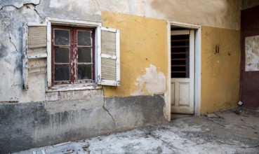 Backyard of a deserted abandoned house with a broken closed window and door and with yellow cracked