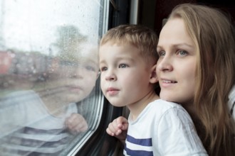 Mother and son looking through a train window as they enjoy a days travel with the small boys face