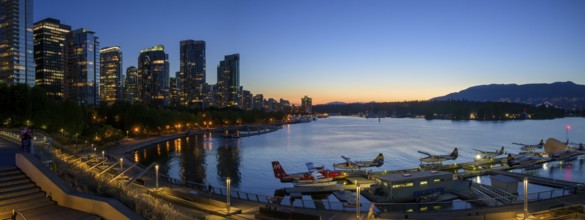 Harbour view at sunset with seaplanes and illuminated skyline in the background, Vancouver, British