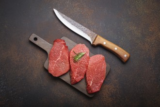 Three raw uncooked meat beef top sirloin steaks on wooden cutting board with rosemary on wooden