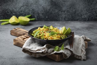 Asian vegetarian noodles with vegetables and lime in black rustic ceramic bowl, wooden chopsticks