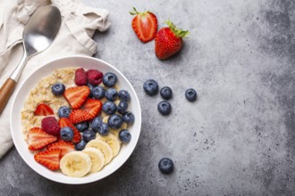 Oatmeal porridge with fruit and berries in bowl with spoon on gray stone background table top view,