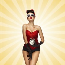 Sexy pinup girl in a red vintage corset holding a retro alarm clock and posing on colourful