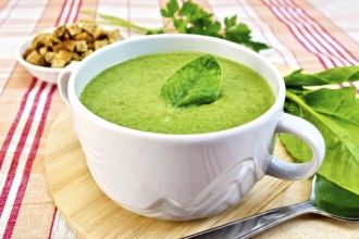 Green soup puree in a bowl with green leaf spinach, spoon on the board, croutons, parsley on a