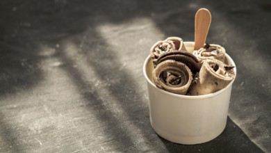 Rolled ice cream with in cone cup on dark rustic background. Iced rolls with biscuits chocolate
