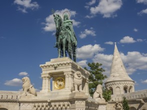 Equestrian statue with lions and a surrounding tower in front of a blue sky, budapest, danube,