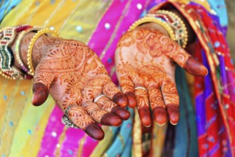 Close-up of painted hands with elaborate mehndi designs, accompanied by colourful robes, Rajasthan,
