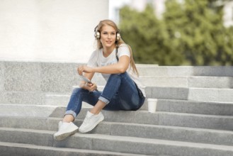 Happy young woman with vintage headphones and a cup of coffee to go, surfing the internet on a