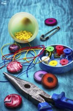 Beads, pliers and other needlework accessories on outdated turquoise wooden background