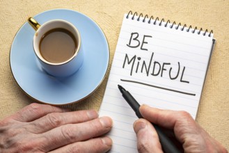 Be mindful - man hand writing a note with a black marker in a spiral notebook