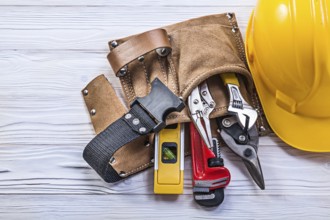 Collection of construction tooling in leather tool belt safety building helmet on wooden board