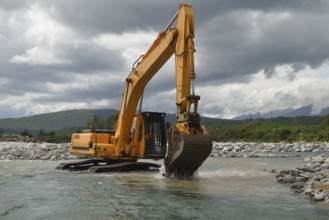 10 ton digger shifting shingle to deepen the channel in a flowing river, Westland, New Zealand,