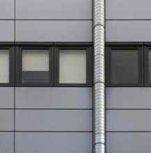 Grey cladding panels on an industrial building with a row of back window frames and a silver pipe