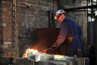 A foundryman clears slag from the molten iron in the furnace