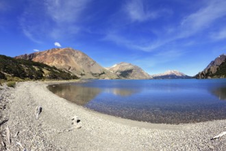 Oval blue lake surrounded by mountains. Mountains reflected in the mirrored water. Picture taken