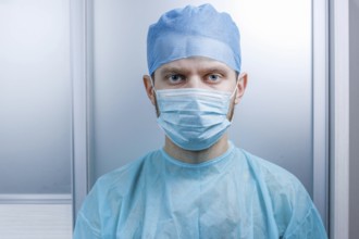 Doctor facing the camera, dressed in mask and scrubs in a clinical setting